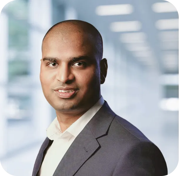 Portrait of a confident bald man wearing a dark suit jacket and white shirt in a bright office setting.