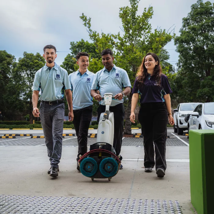 Two janitors in navy uniforms cleaning a modern office lobby; one mopping the floor and the other wiping the glass reception desk.