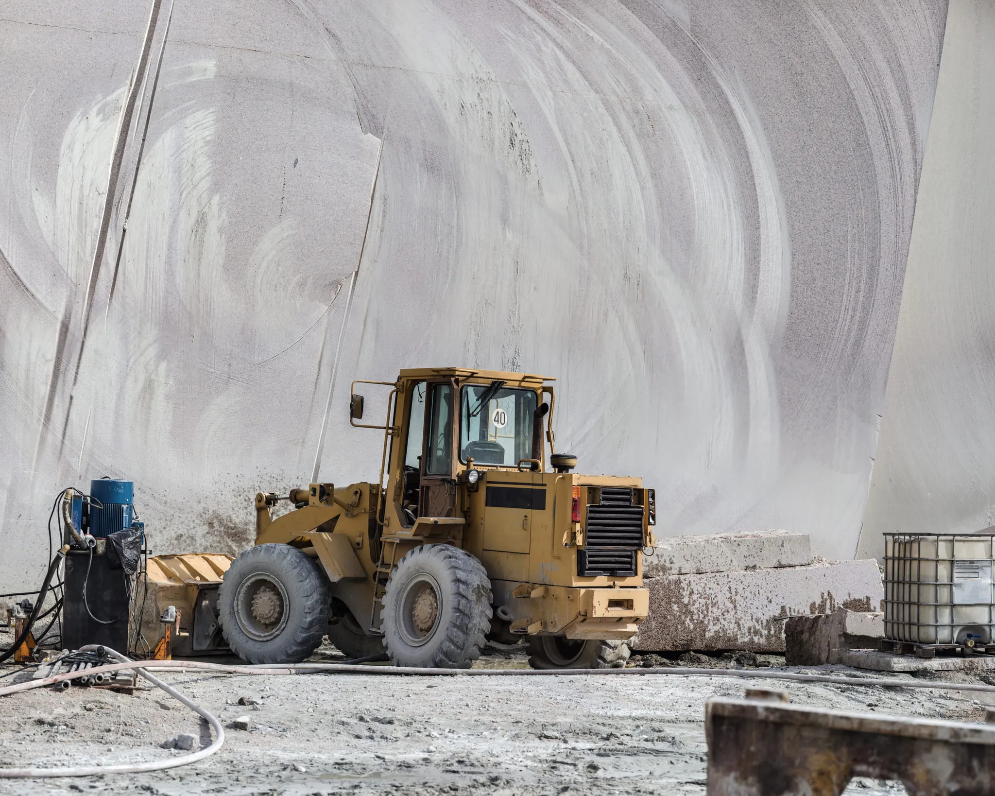 Yellow heavy machinery vehicle at a quarry site with large stone blocks in the background.