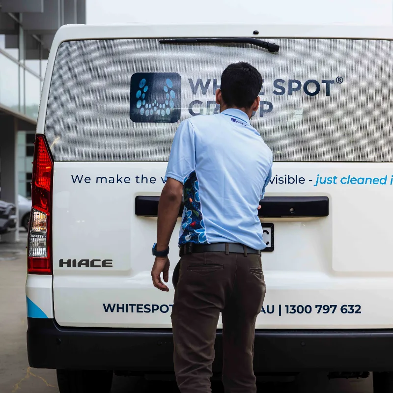 Person in blue shirt standing behind a Whitespot Group van that has contact information and the phrase 'We make the visible just cleaned'.