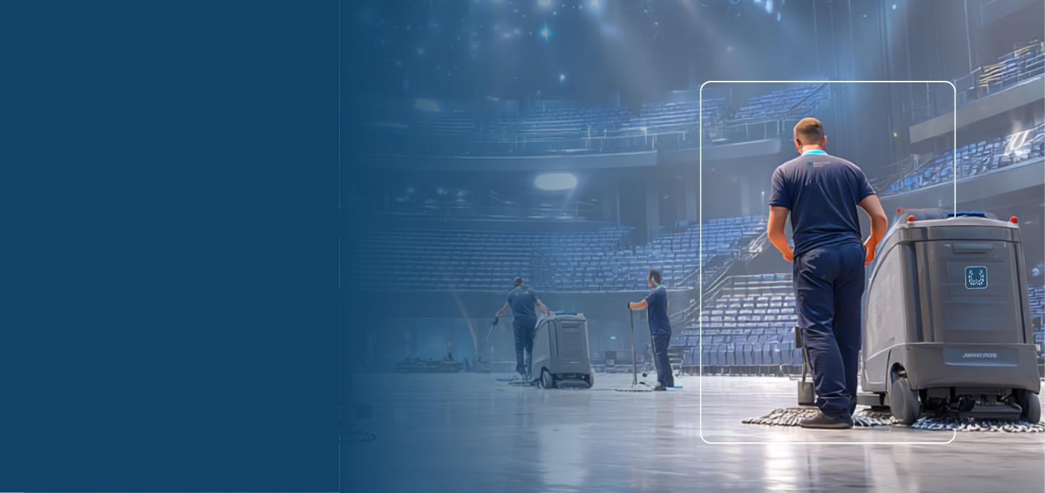 Cleaning staff operating floor cleaning machines in a large, empty indoor arena with tiered blue seats.