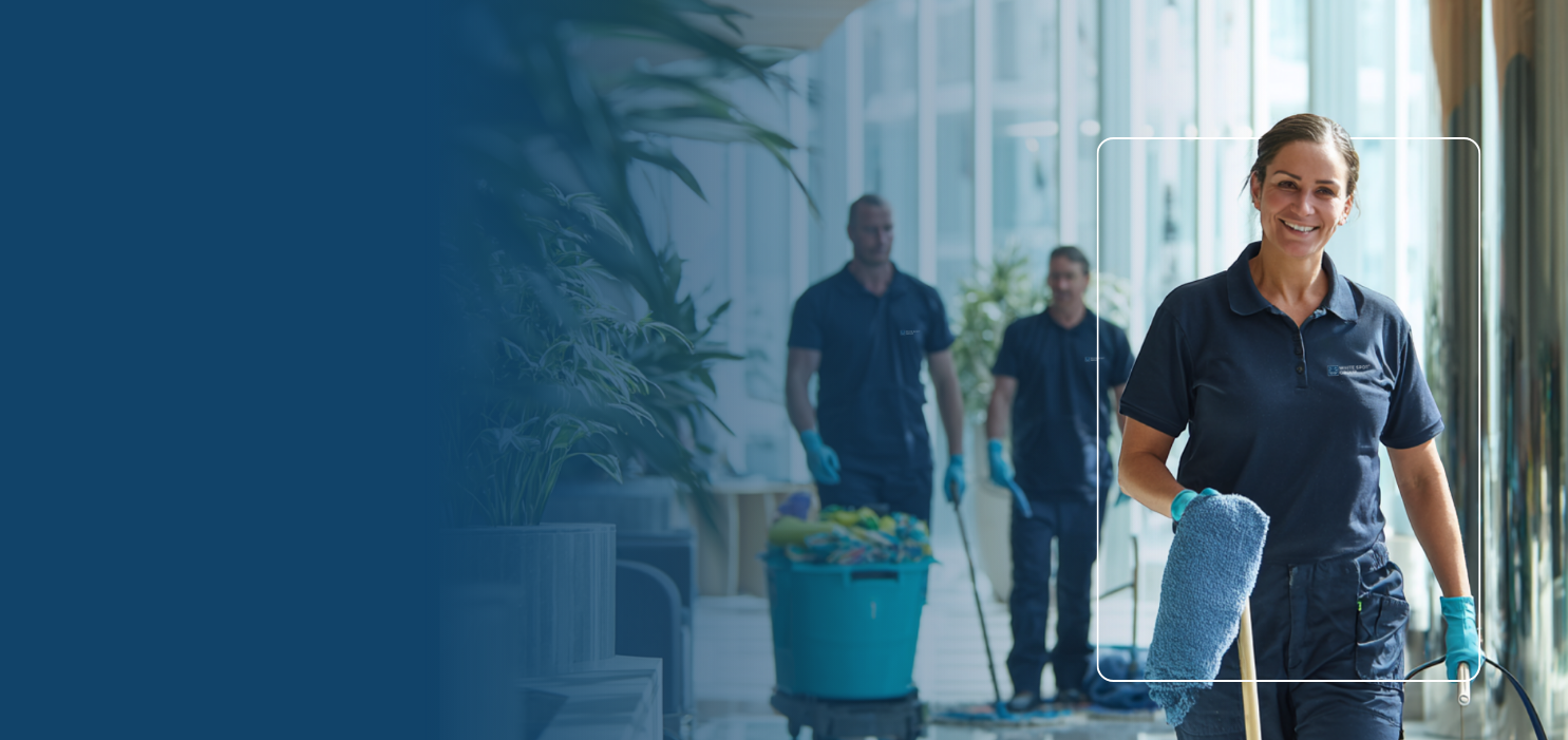 Smiling female cleaner in navy uniform holding cleaning mop, with two male colleagues and a bucket in a bright corridor.