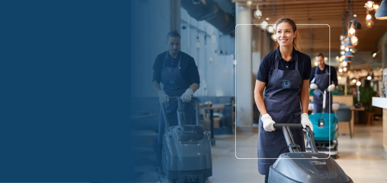 Three janitors smiling and pushing floor cleaning machines in a well-lit commercial space.