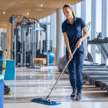 Woman cleaning gym floor with a mop in a fitness center.