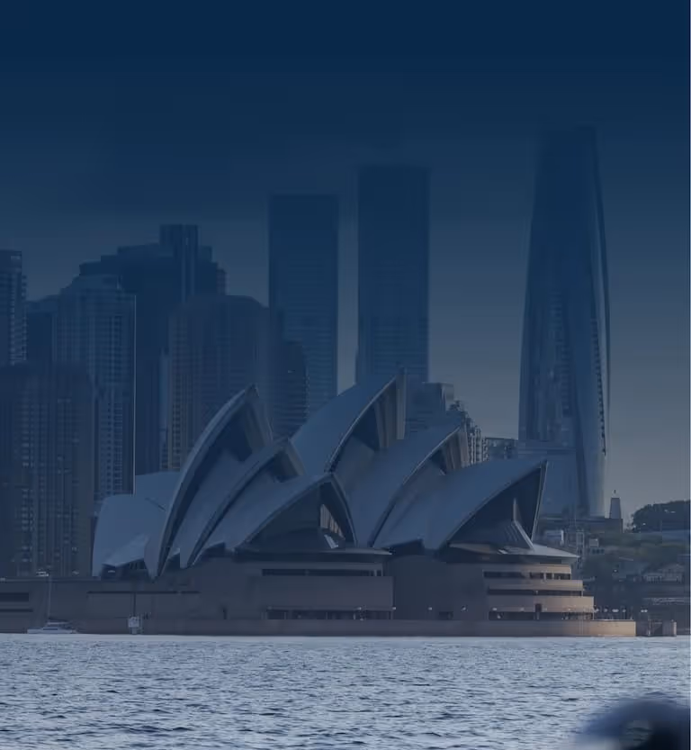 Sydney Opera House with city skyscrapers in the background across the harbor water.