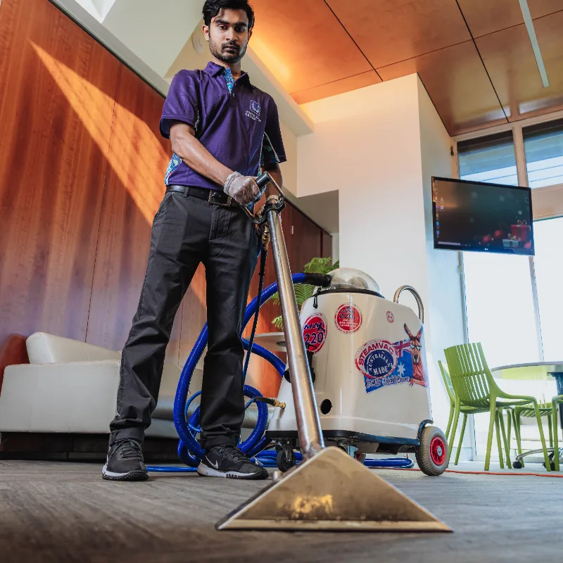 Worker using a commercial steam cleaning machine to clean a carpet in a modern office space.
