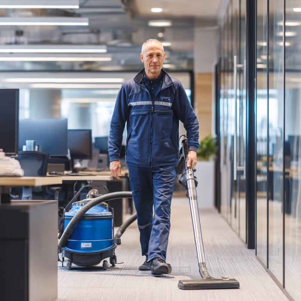 Professional cleaner vacuuming carpeted floor in modern office space.