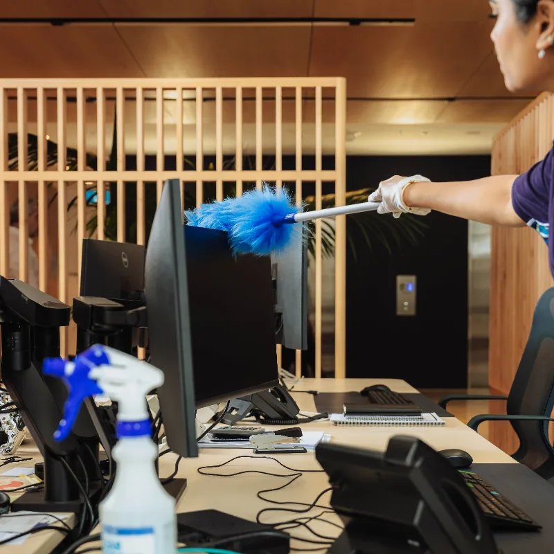 Person dusting the top edge of a computer monitor with a blue duster in a modern office.