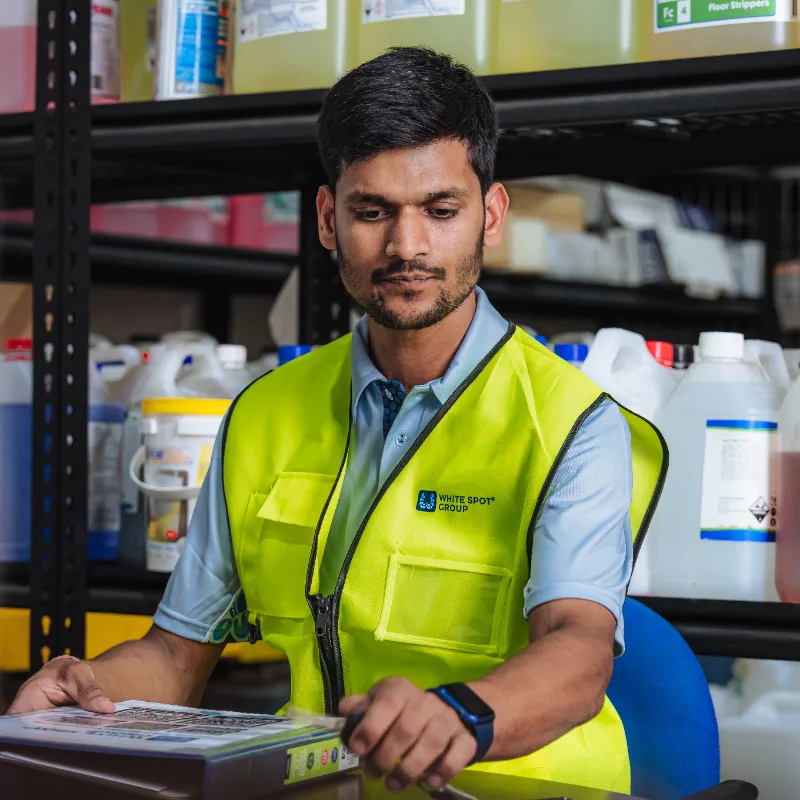 Man in a yellow safety vest sitting at a desk and looking at a binder in an industrial storage room.