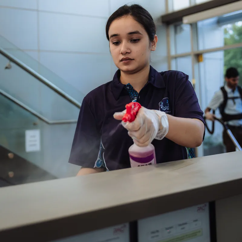 Woman wearing gloves disinfecting a surface with spray bottle in a modern indoor space.