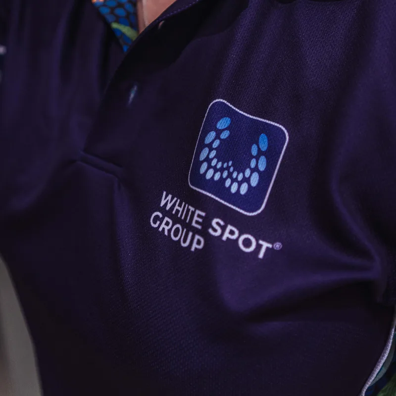 Close-up of a dark purple shirt with the White Spot Group logo featuring a blue and light blue dotted design.
