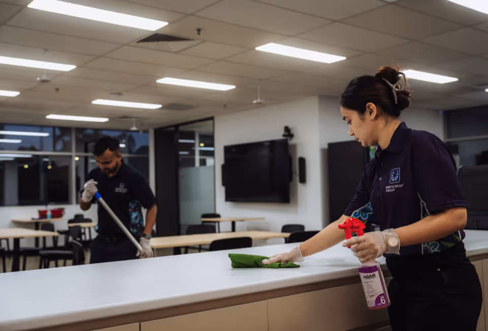 Two janitors in uniform cleaning a modern classroom with a mop and a spray bottle with cloth.