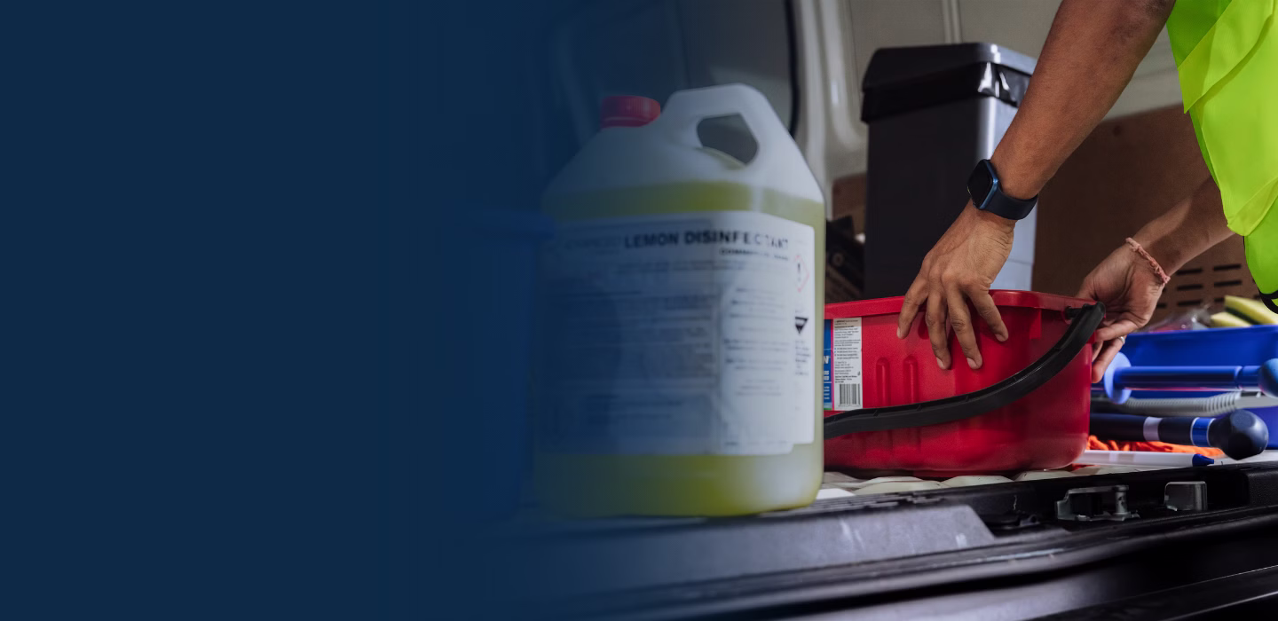 Person in a safety vest handling a red toolbox among cleaning supplies inside a vehicle.