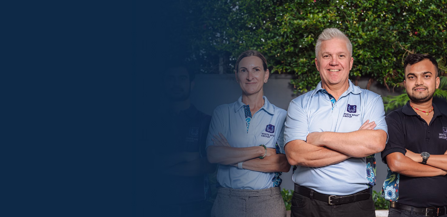 Three smiling professionals standing outdoors with folded arms, wearing White Spot Group shirts.