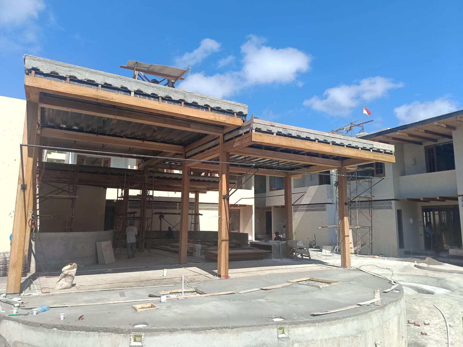 Construction site of a modern building with wooden beams, scaffolding, and concrete foundation under a blue sky.