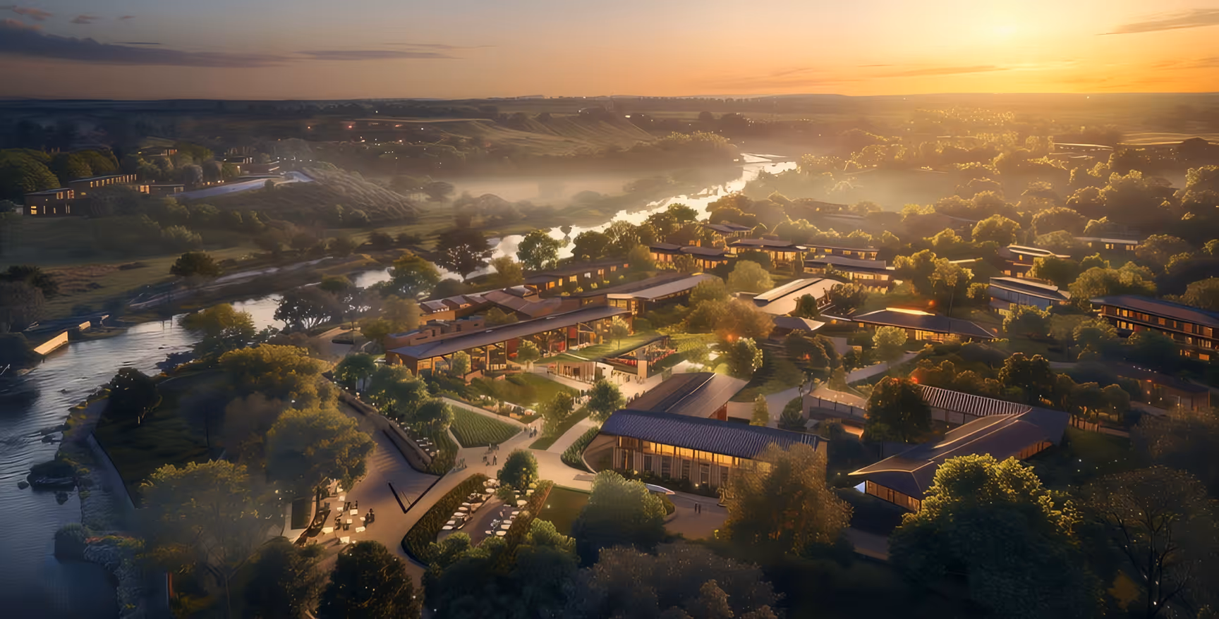 Aerial view of a modern riverside community at sunset with landscaped gardens, walking paths, and contemporary buildings surrounded by trees.