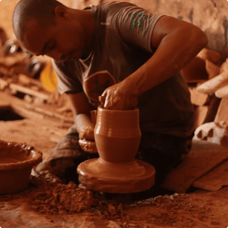 Man shaping clay pot on a pottery wheel in a warm-toned workshop.