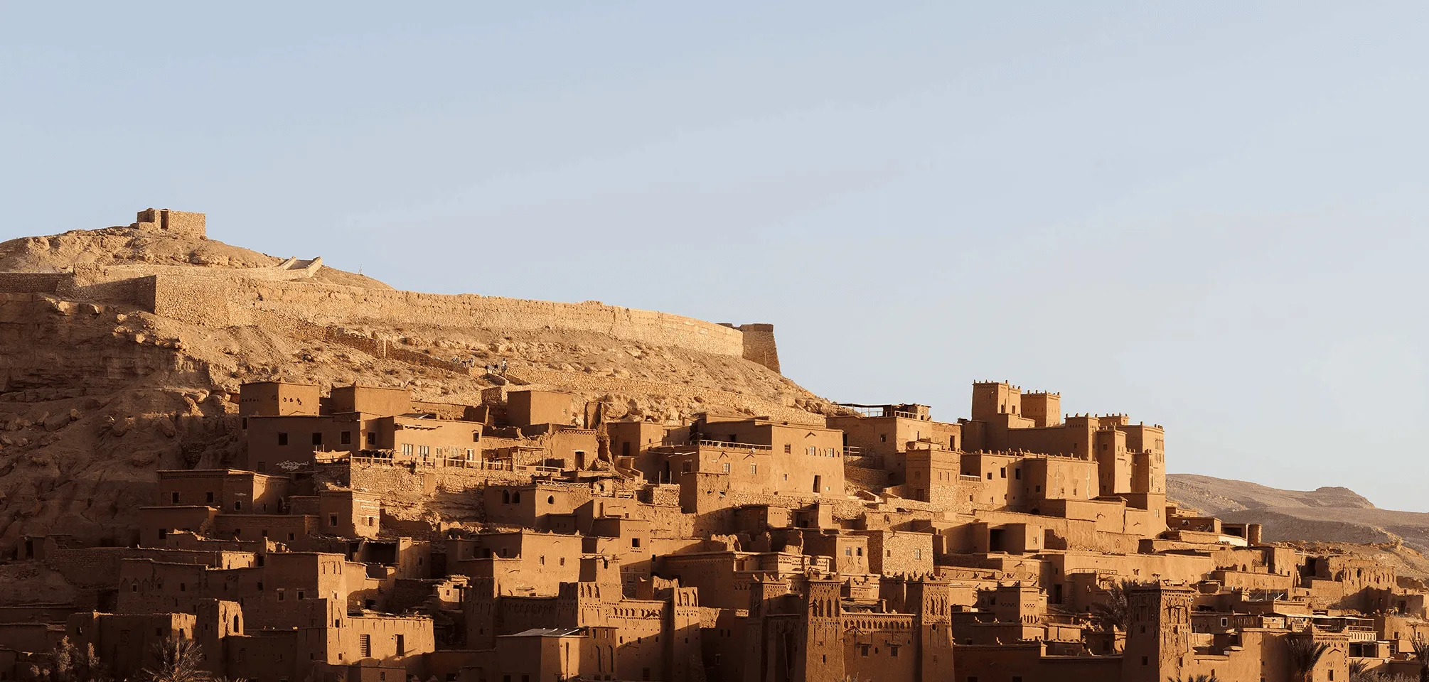 Ancient mud-brick buildings on a hillside under a clear sky at sunset.