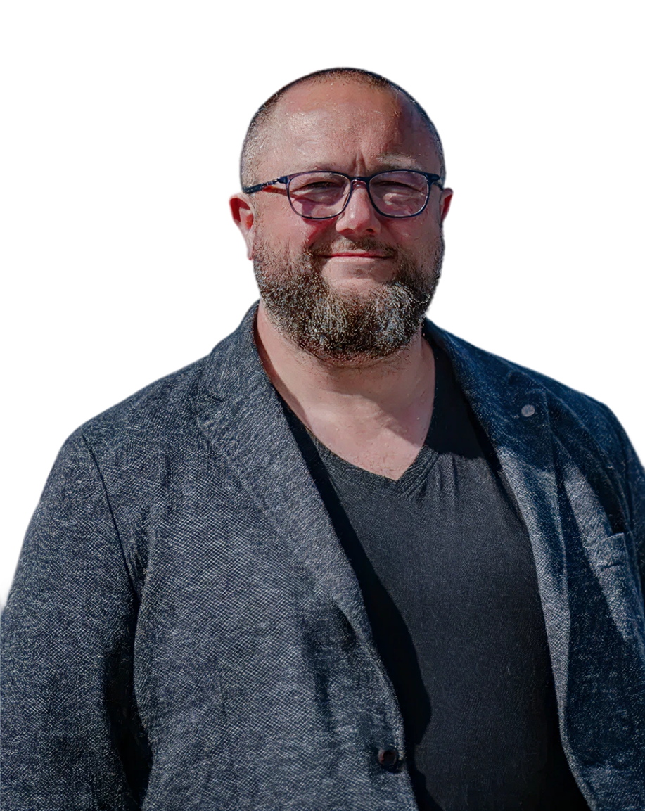 Ältere Frau mit Brille sitzt lächelnd am Tisch und hält ein Foto in der Hand.