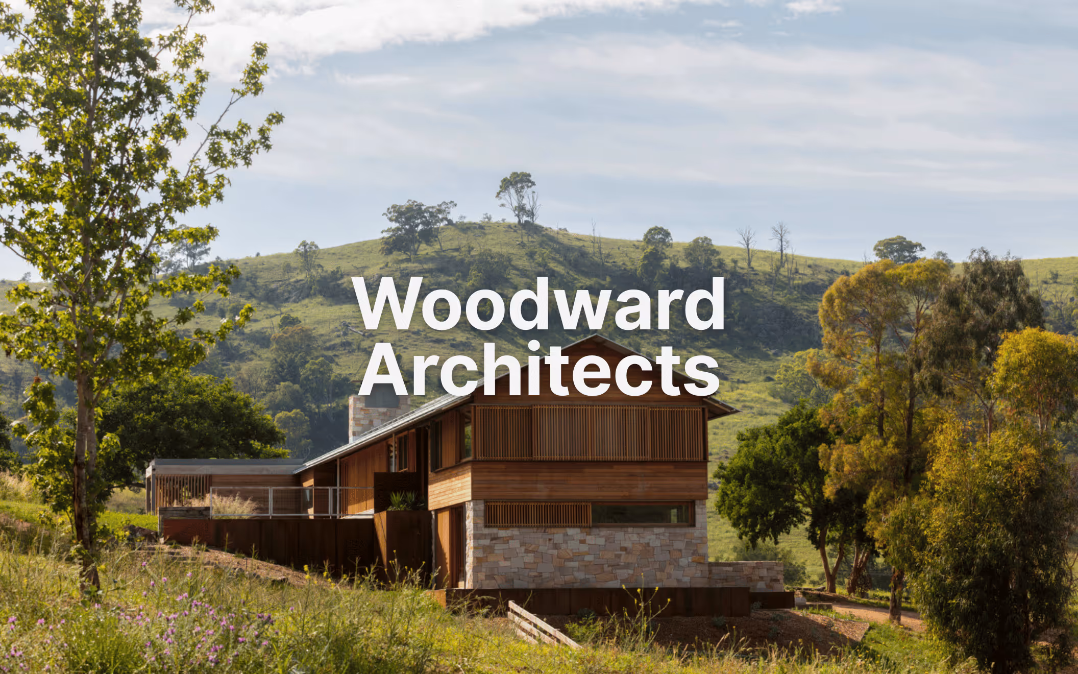 Contemporary two-storey home with timber and stone facade designed by Woodward Architects, set in a lush hillside landscape.