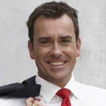 Lächelnder Mann im weißen Hemd mit roter Krawatte, der eine Jacke über die Schulter wirft.