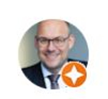 Porträt eines Mannes mit Brille und Anzug, Lächeln, vor neutralem Hintergrund.