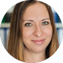 Porträt einer lächelnden Frau mit langen braunen Haaren und grünen Augen.