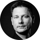 Schwarz-weiß-Porträt eines Mannes mit kurzem Haar vor dunklem Hintergrund.