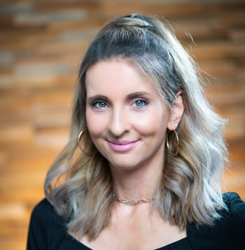 Frau mit halblangem gewelltem Haar, die lächelnd vor einer unscharfen Holzwand posiert.