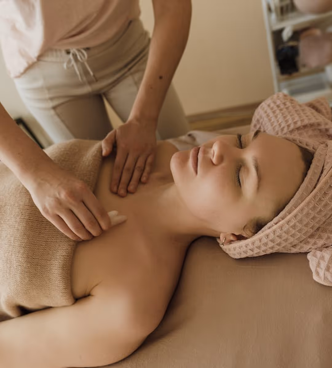 Woman receiving a chest and shoulder massage while lying on a massage table with a towel wrapped around her head.