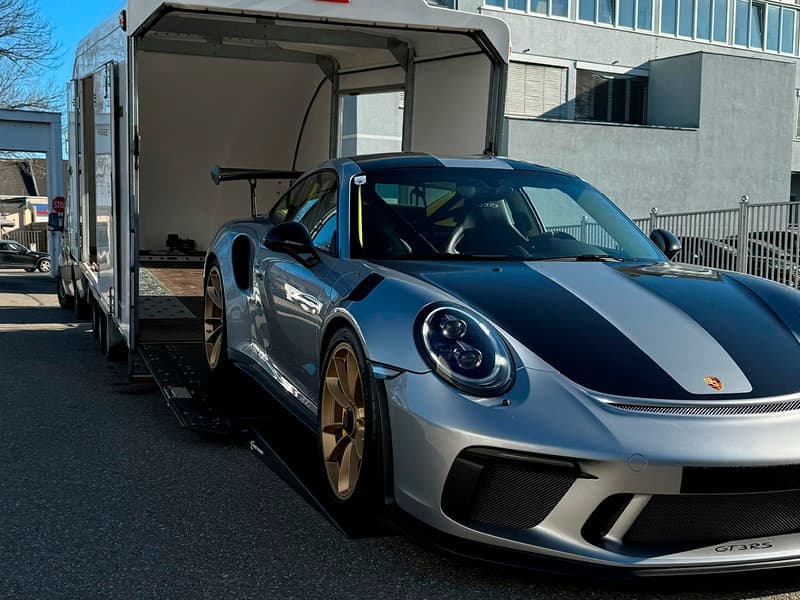 Silver Porsche GT3 RS sports car with gold wheels being loaded into a white enclosed trailer.