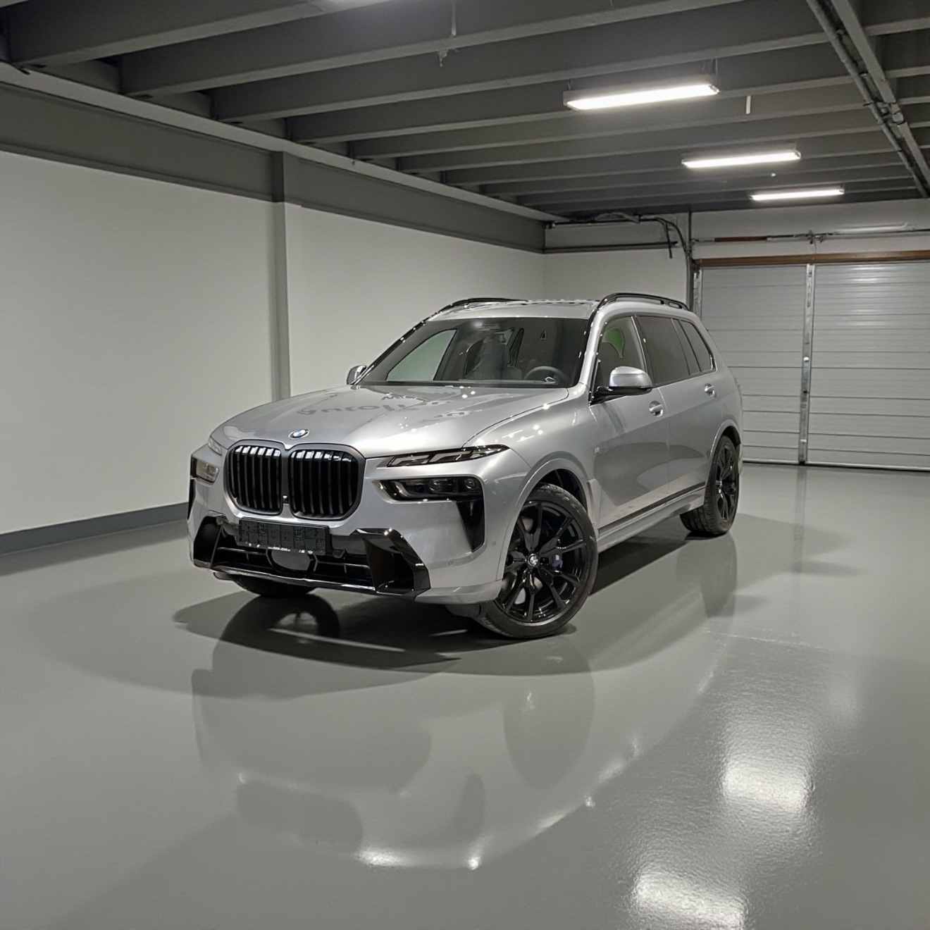 Silver BMW SUV with black wheels parked inside a spacious, empty garage with white walls and overhead lights.