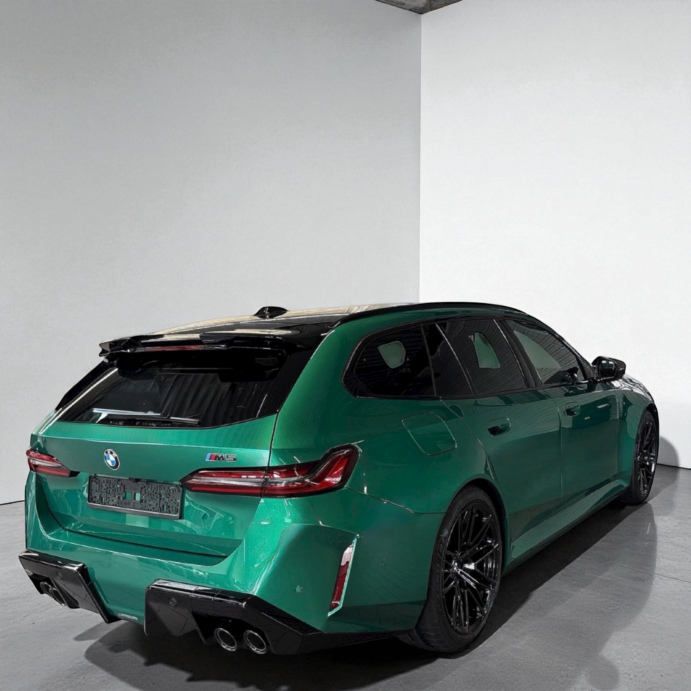 Green BMW M5 touring car with black roof and quad exhausts parked indoors.