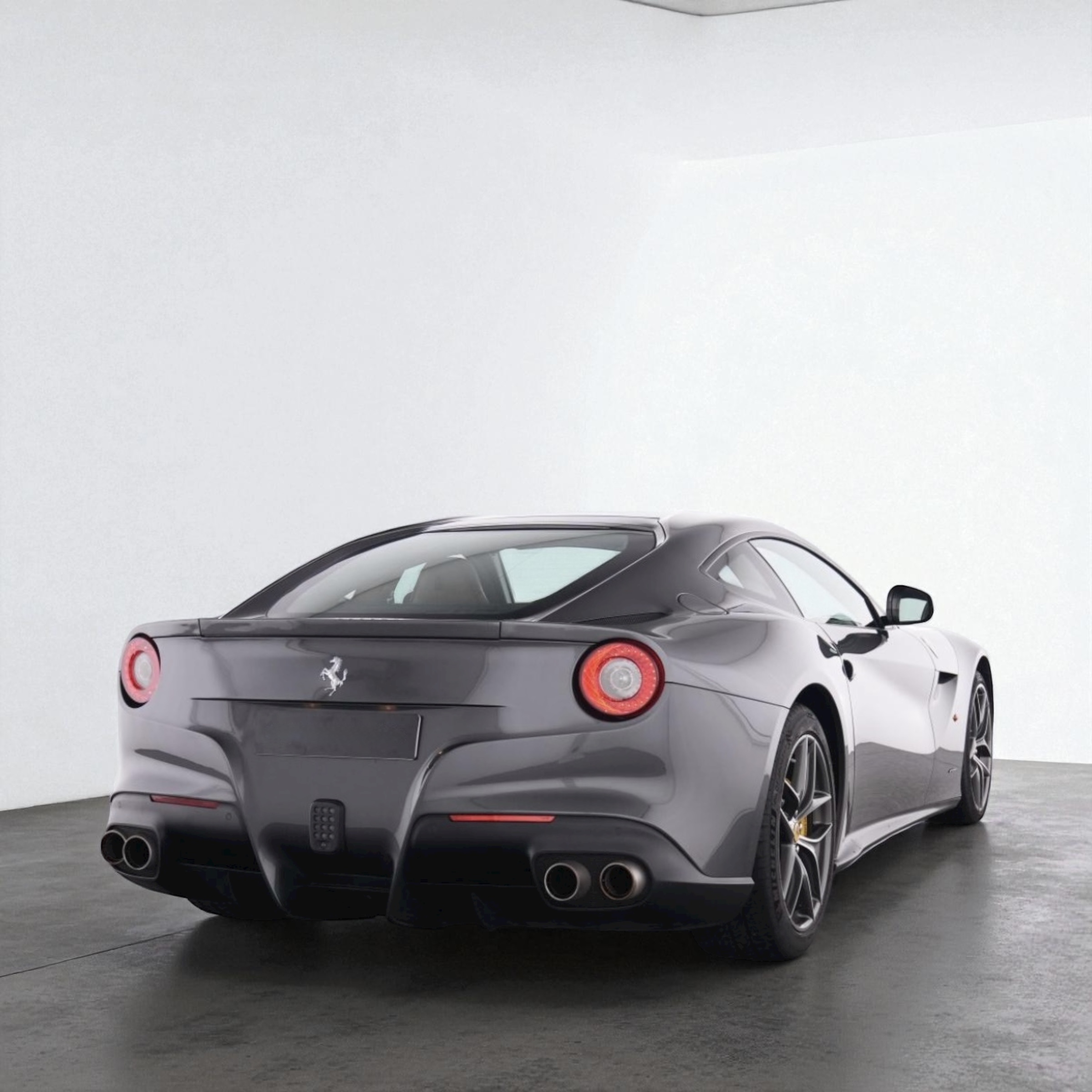 Rear three-quarter view of a sleek gray Ferrari sports car with circular taillights and quad exhaust pipes.