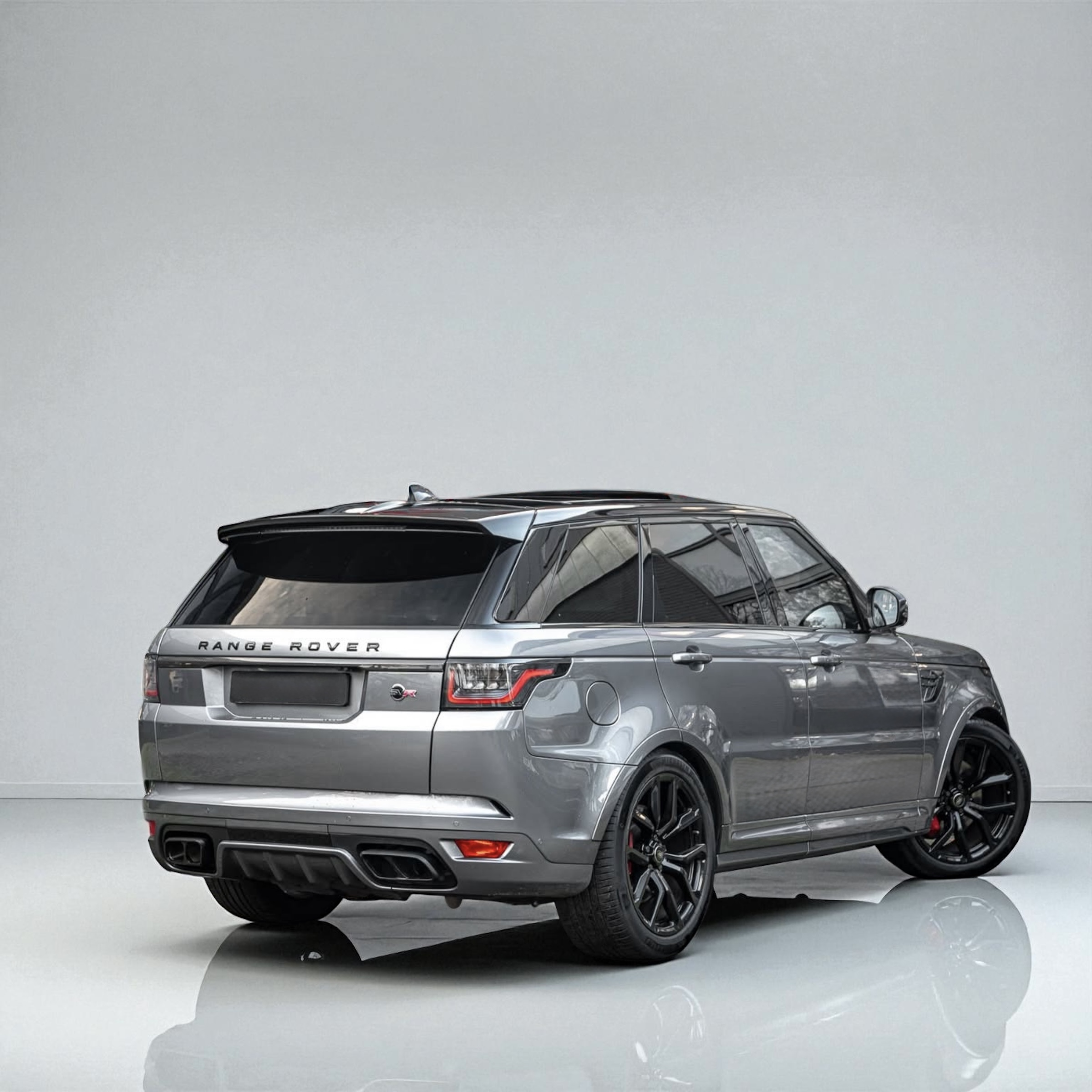 Rear-side view of a silver Range Rover parked on a glossy white floor in front of a plain light gray wall.