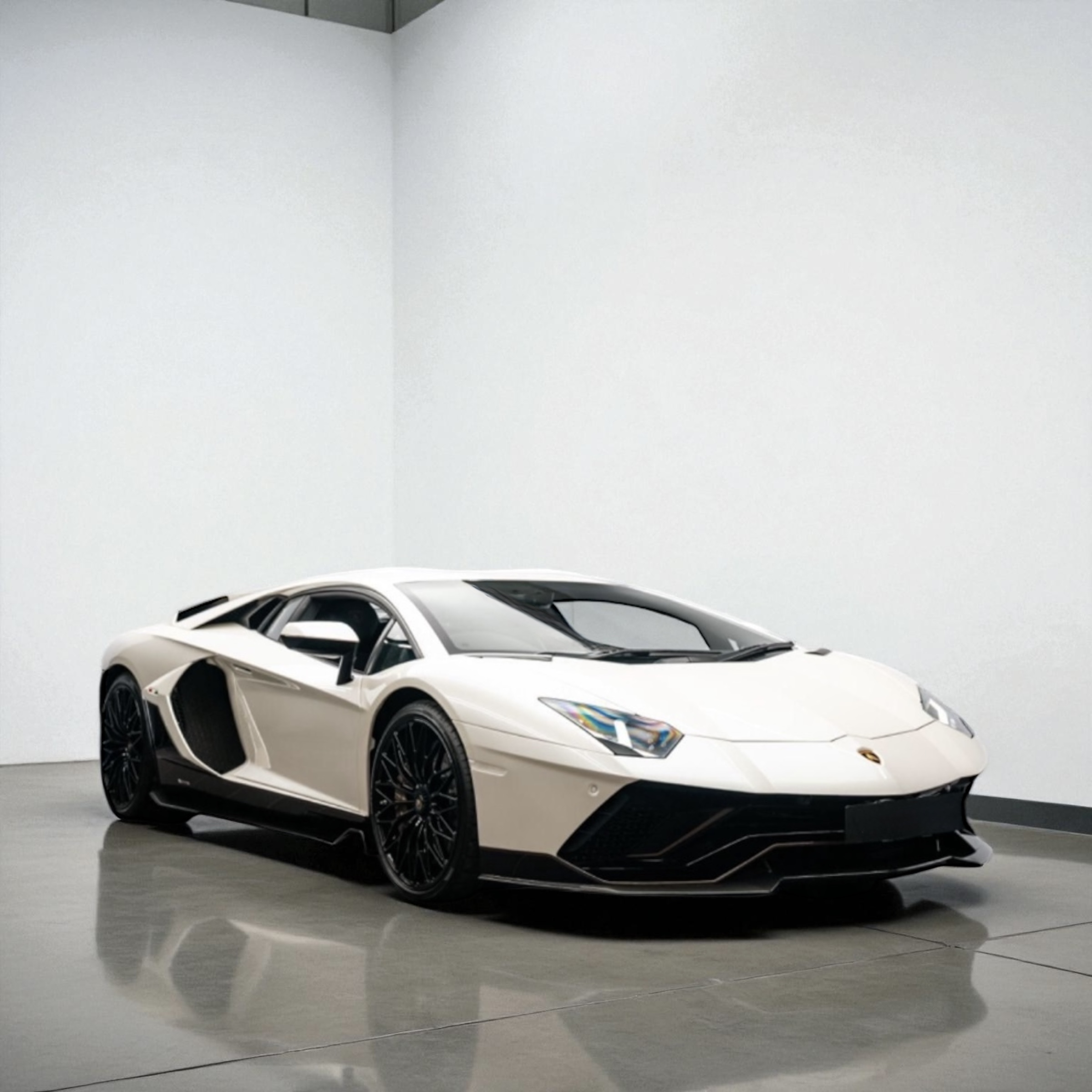White Lamborghini sports car with black rims parked on a polished concrete floor against a plain white wall.