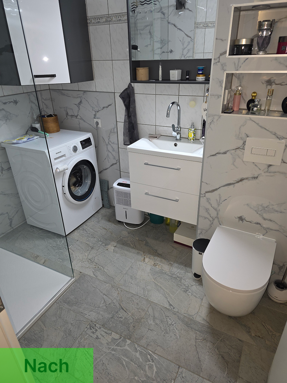 Bodennahe Duschwanne mit begehbarer Glasabtrennung. Neue Wandpaneele in Marmoroptik, Duschsystem mit Regendusche und Handbrause sowie neue Bodenfliesen. Sicherer Einstieg, kein hoher Wannenrand mehr.