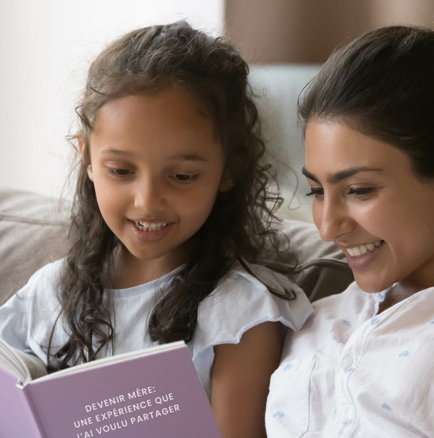 Mère et fille souriantes lisant un livre Ma vie en LIVRE ensemble sur le canapé.