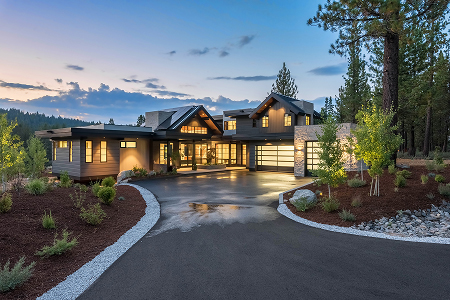Modern luxury house at dusk with illuminated large windows, surrounded by trees and landscaped front yard.