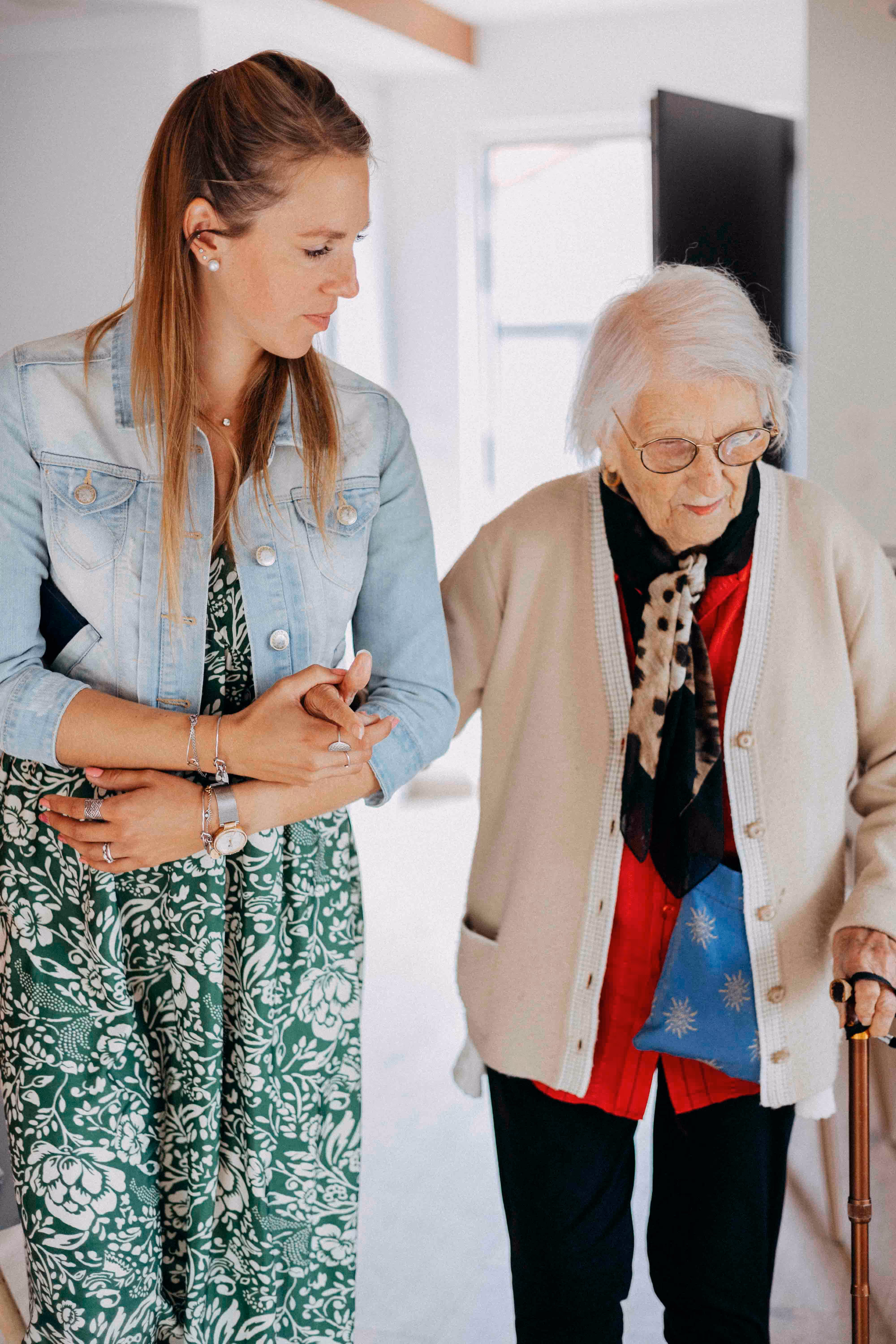 Une femme jeune aide une femme âgée tenant une canne à marcher à l'intérieur.