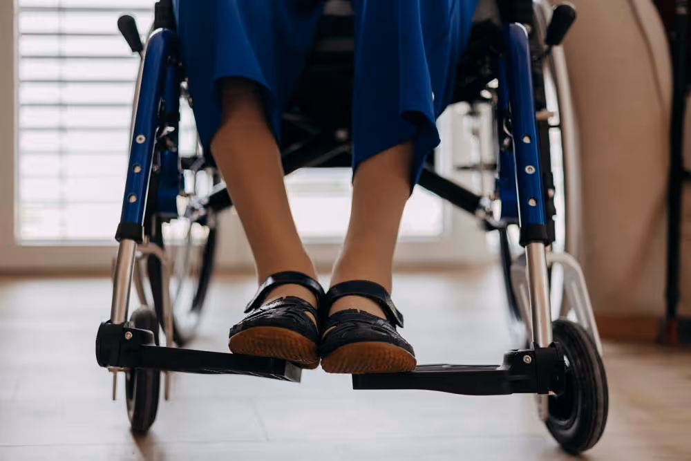 Pieds d'une personne assise dans un fauteuil roulant posé sur les repose-pieds.