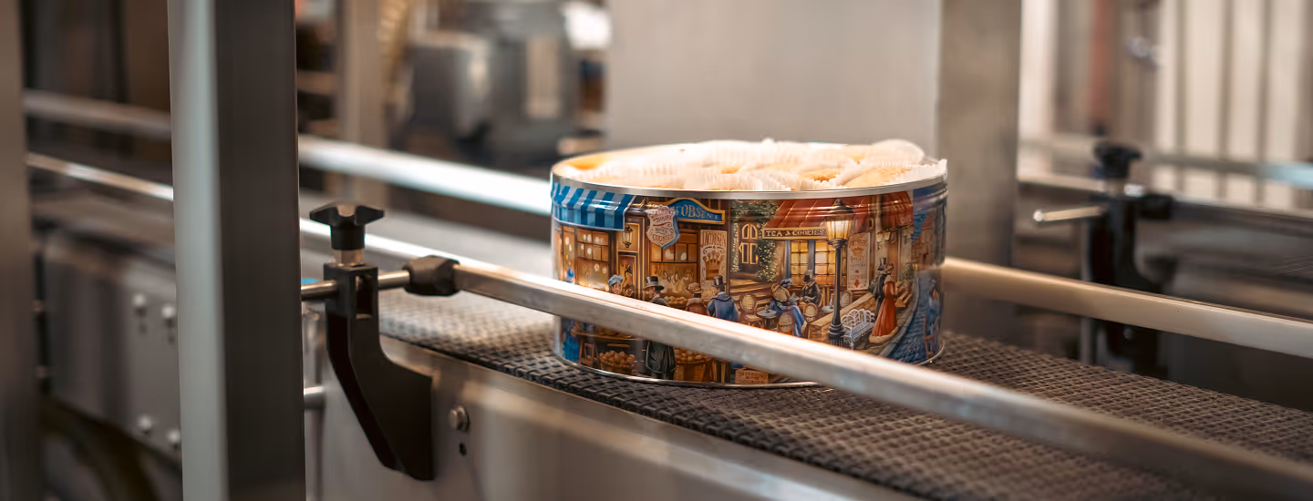 Decorative tin filled with pastries on a conveyor belt in a bakery packaging line.