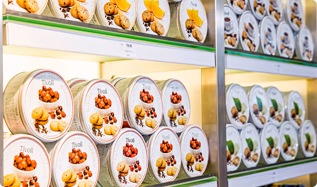 Shelves stocked with round cookie tins labeled Tivoli, featuring images of cookies and fruit on the packaging.