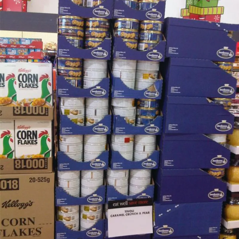 Stacked blue Jacobsens cookie tins beside cereal boxes in a store in Canada