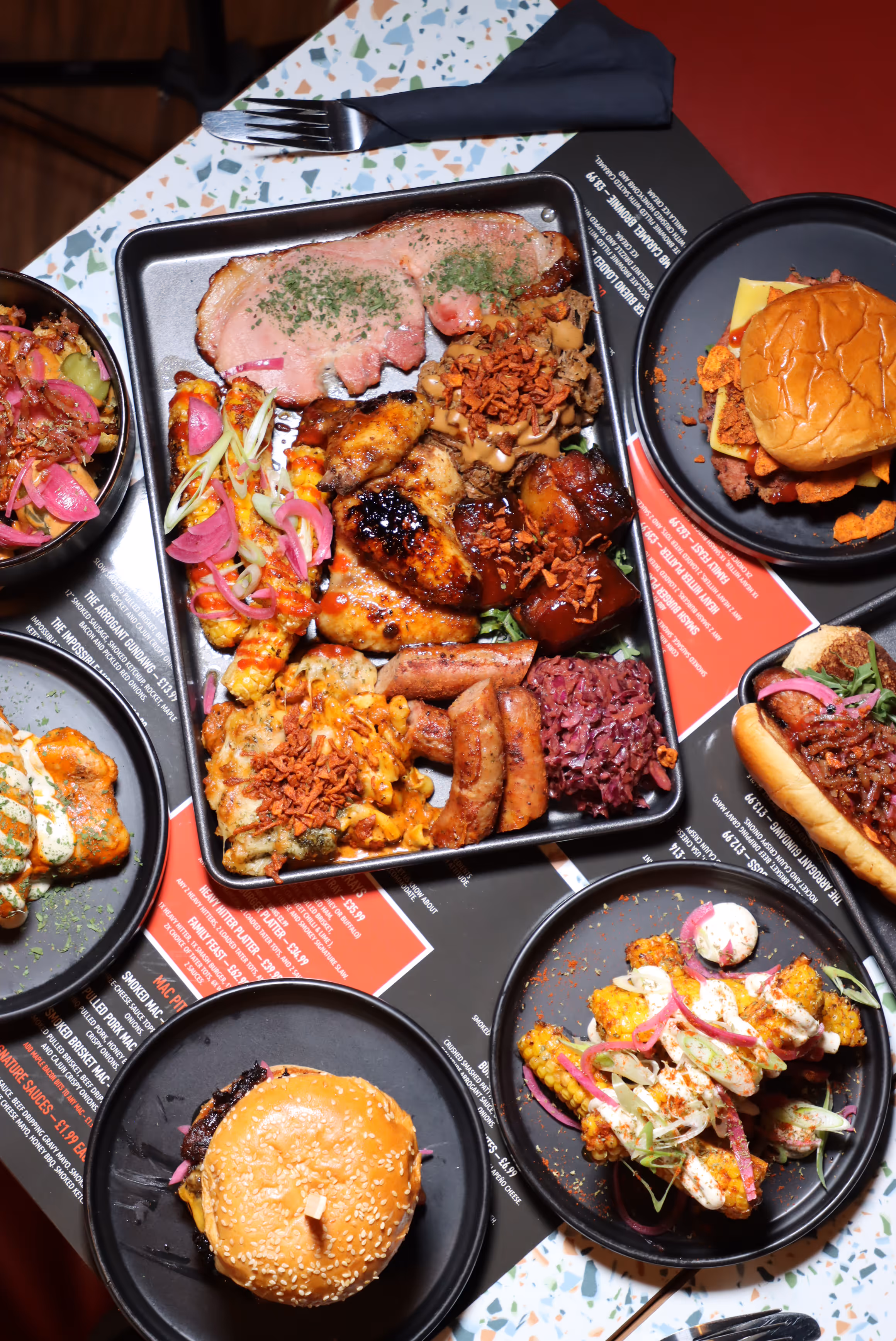 Variety of grilled and smoked meats, including ribs, chicken wings, sausages, and burgers, served on plates and tray with garnishes and sauces.