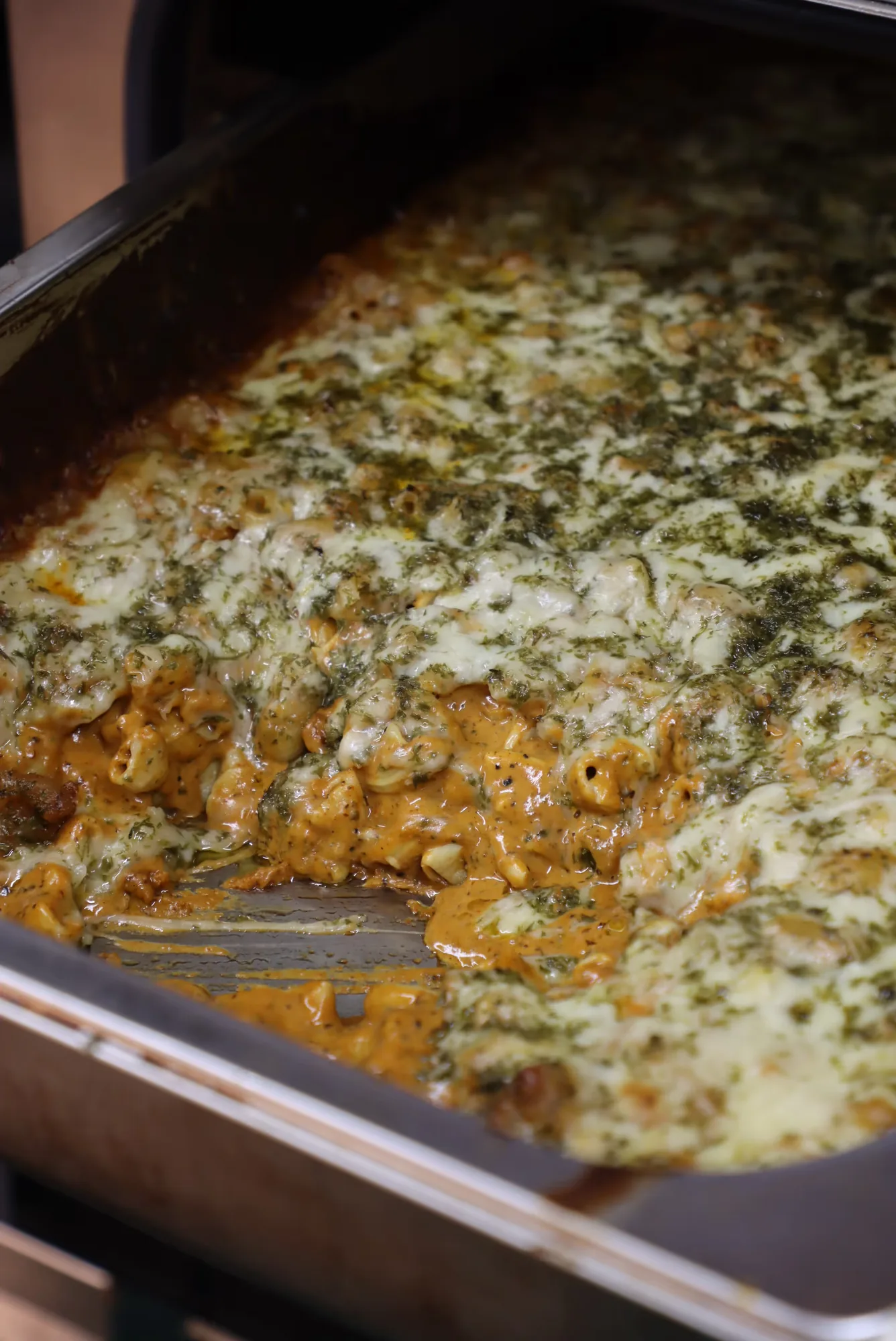 Baked cheesy pasta casserole with creamy sauce and herbs in a metal baking tray.