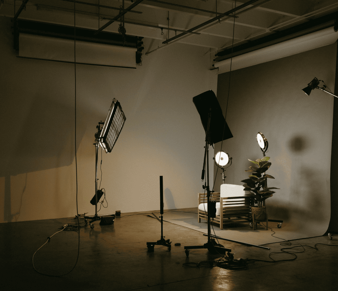 Studio photo avec éclairages professionnels, fond gris, fauteuil et plante, illustrant la mise en place d’un éclairage en photographie.