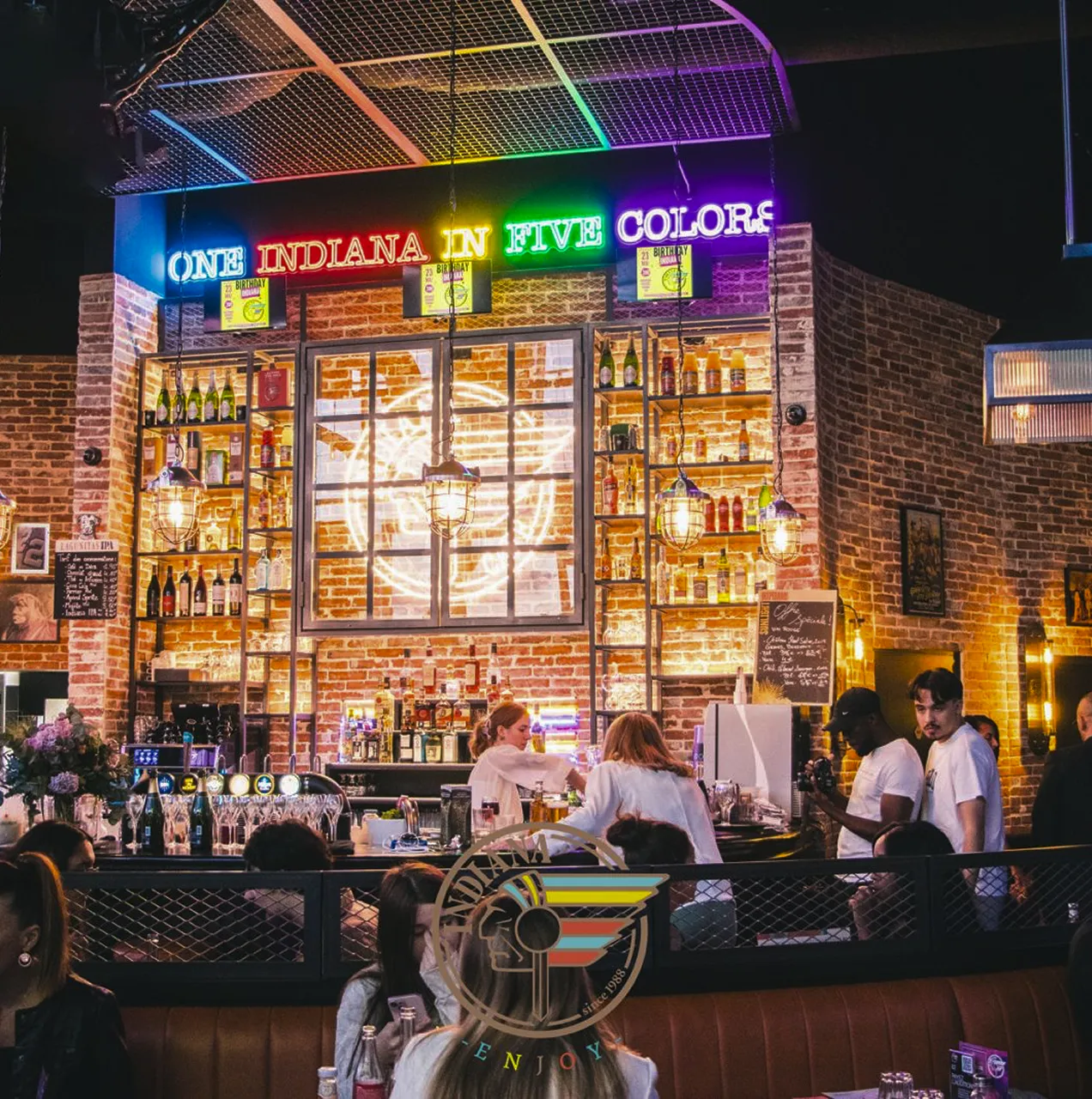 Bar animé d’un restaurant Indiana Café avec mur en briques, néon coloré et équipe en service