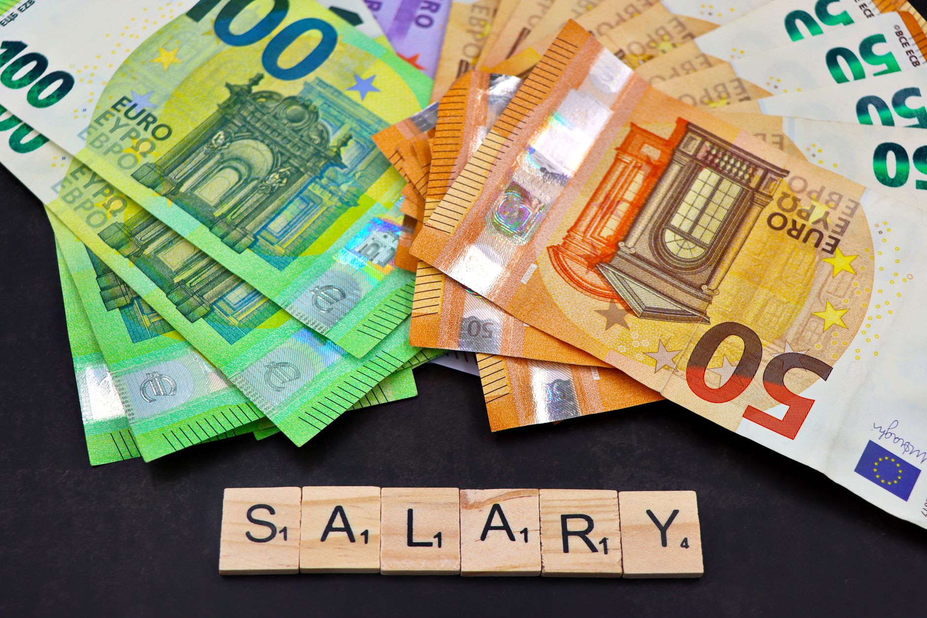 Euro banknotes alongside wooden Scrabble letters spelling 'salary' symbolize financial earnings and payroll.
