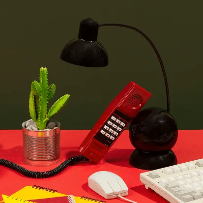 A vintage red telephone, black lamp, potted succulent, and computer accessories on a vibrant red desk.